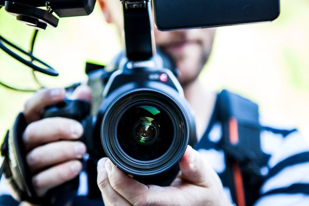 person-holding-canon-dslr-camera-close-up-photo-320617 A close-up shot of a cameraman filming, focusing on the camera lens and equipment.