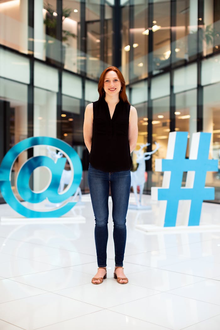 programs-01 Confident young woman standing in a modern office atrium with digital symbols.
